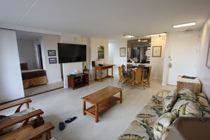 Ein Wohnzimmer mit Couch, einem Couchtisch aus Holz, einem Essbereich mit Holztisch und Stühlen sowie einem an der Wand montierten Fernseher.