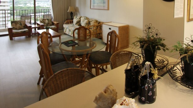 A spacious living room with a balcony, furnished with wicker chairs and a sofa, and a dining area with a glass table. - Upgraded 1BR Condo Ocean View - Kitchen, FREE parking, WiFi (Honolulu)