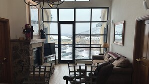 Un salon chaleureux avec une cheminée, une grande fenêtre donnant sur un paysage enneigé, un canapé confortable et un coin repas avec une table.
