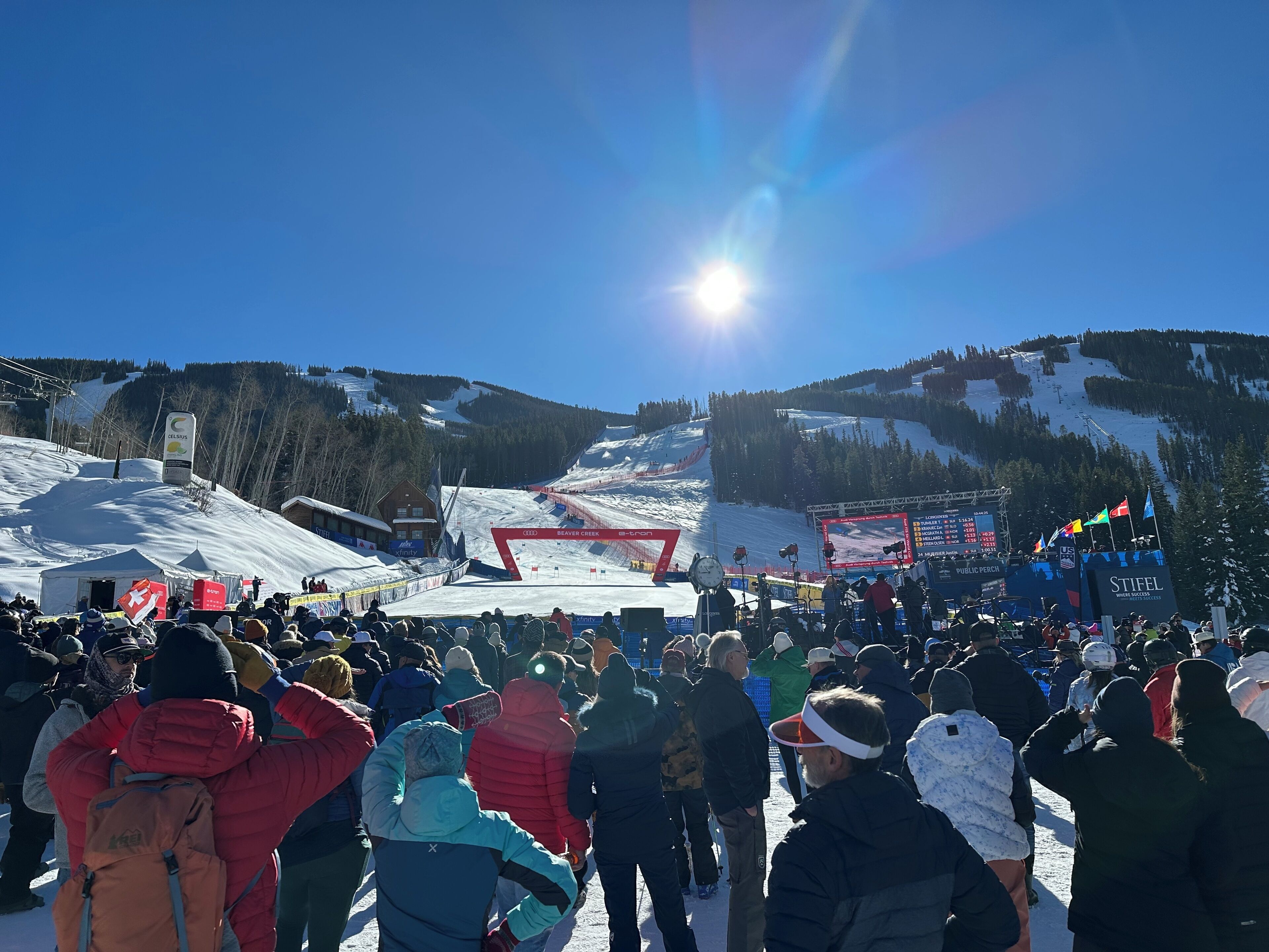 Ein Skigebiet mit einer Menschenmenge am Hangfuß, einer Seilbahn im Hintergrund und einem strahlend blauen Himmel.