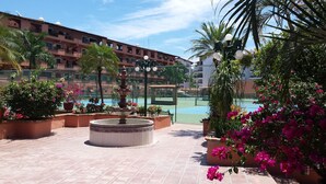 En gårdhave med en springvand, plantekasser og en tennisbane i baggrunden.