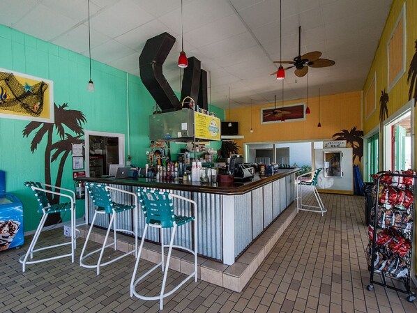 Zona de bar con mostrador, sillas verdes y un ventilador de techo.