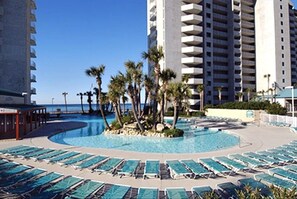 Zona de piscina de un resort con sillones de descanso y palmeras, rodeada de edificios altos.
