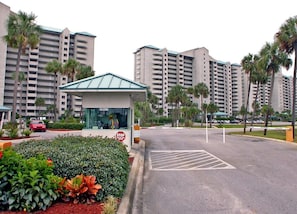 Entrada de hotel con un área de espera techada, palmeras y estacionamiento.