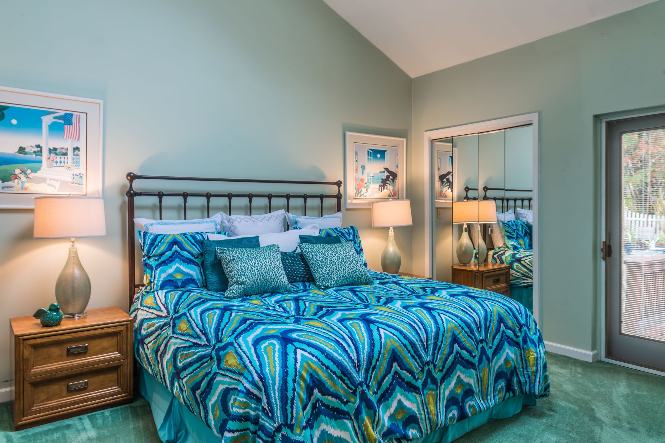 A bedroom with a bed, nightstands, lamps, and framed artwork on the walls.