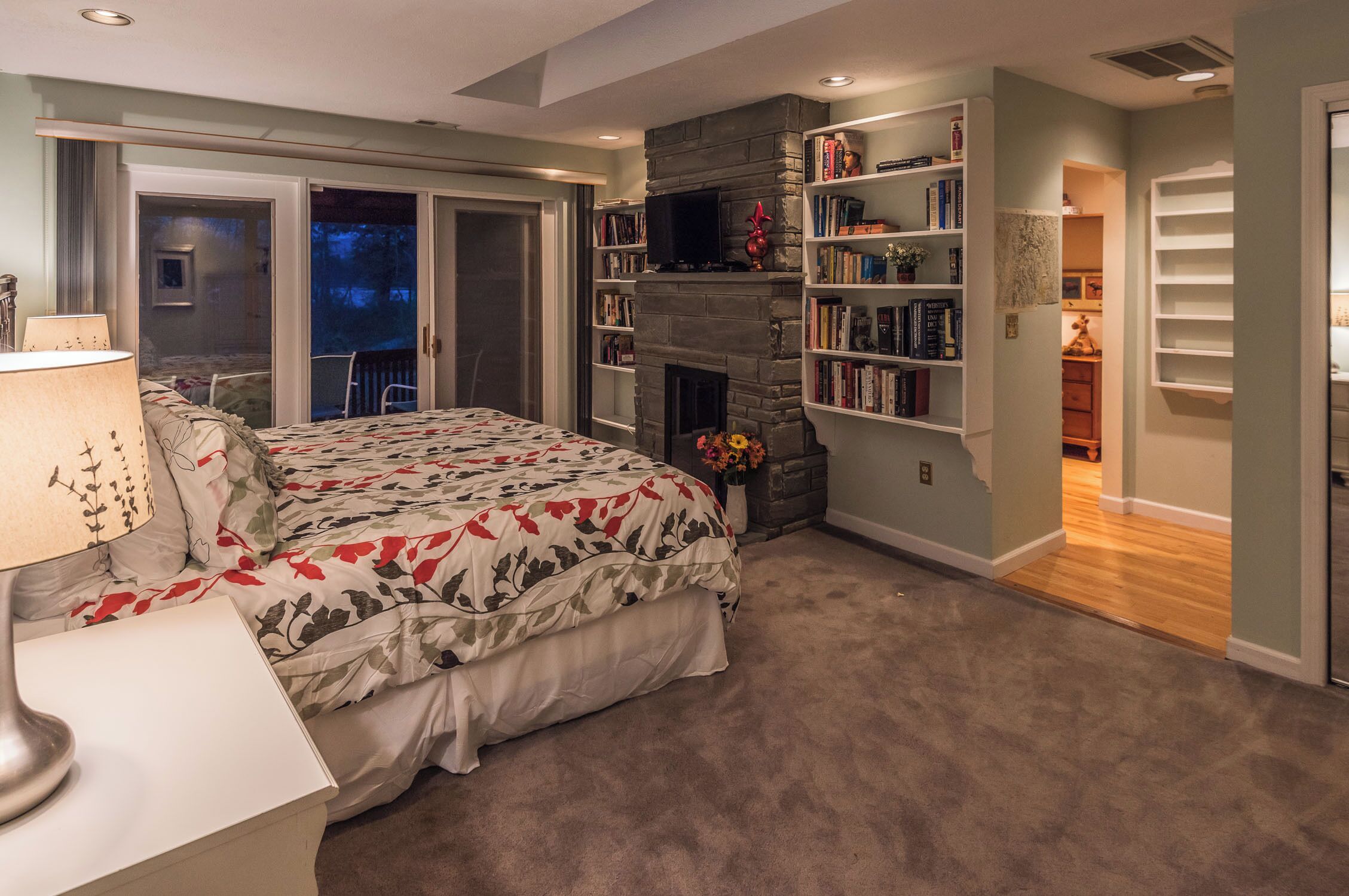 A bedroom with a bed, a fireplace, a bookshelf, and a door leading to a balcony.