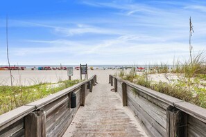 Een houten looppad dat naar een strand leidt, met parasols en borden.