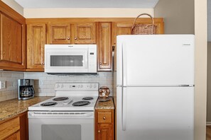 A kitchen with wooden cabinets, a white microwave, a white refrigerator, a stove, and a coffee maker. - Shoalwater 906 Gulf-Front Corner Condo with Beach Views! 3 bedrooms (Orange Beach)