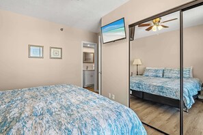 A bedroom with a bed, a ceiling fan, a TV, and a bathroom with a toilet and sink. - Shoalwater 906 Gulf-Front Corner Condo with Beach Views! 3 bedrooms (Orange Beach)