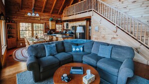A cozy cabin interior with a wooden staircase, a sectional sofa, a dining area, and a kitchen. - Serenity on Cedar-Lakefront Cabin- 10 boats-Swim/Fish/Boat, Starlink & Hulu Live (Tuckasegee)