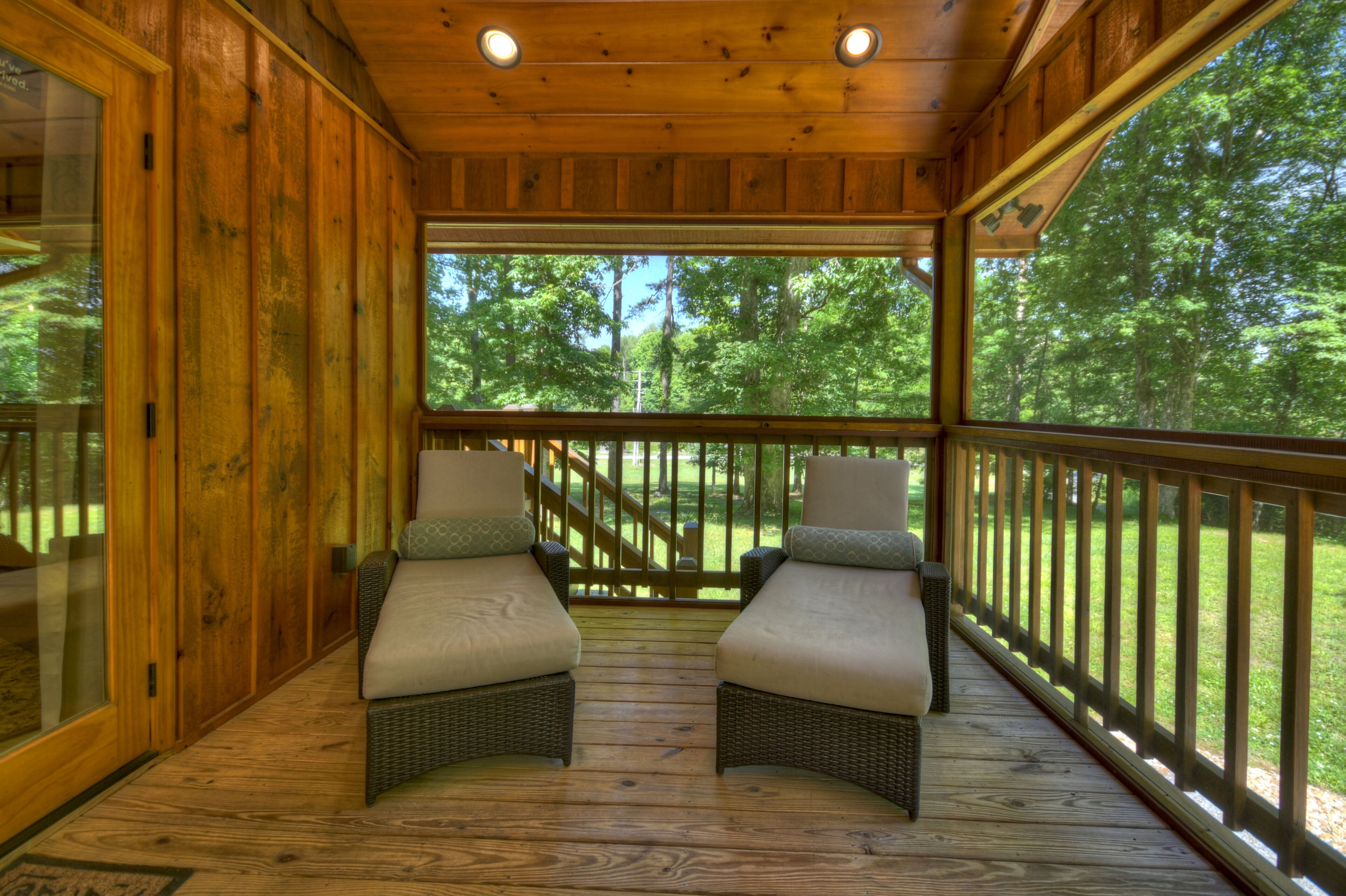A wooden deck with two wicker chairs and a view of a forest.