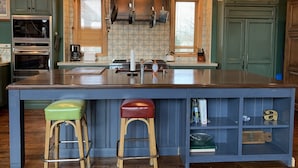 A kitchen with a large island, wooden stools, a built-in bookshelf, and pendant lighting.