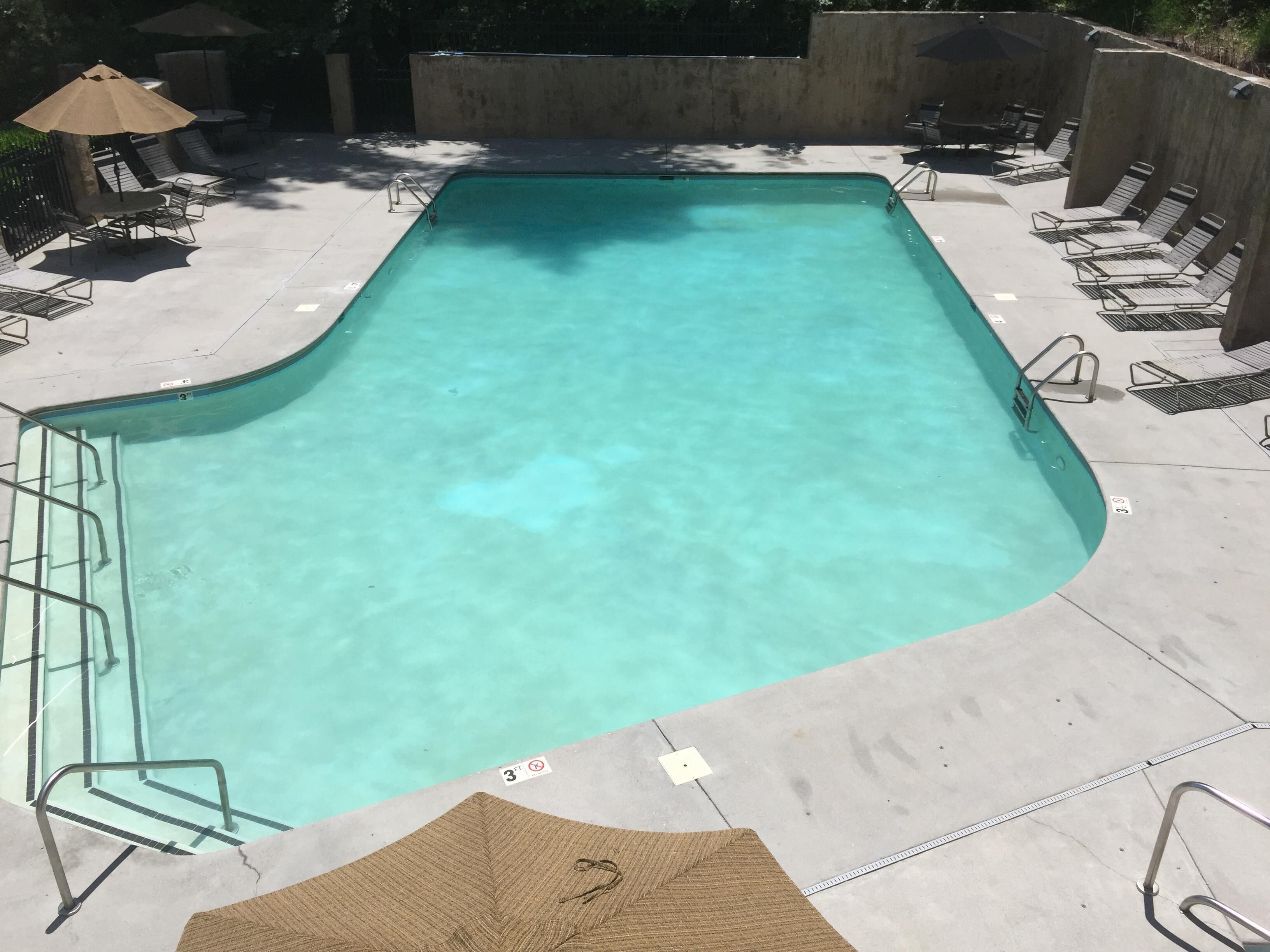 A rectangular swimming pool with clear water, surrounded by lounge chairs and umbrellas.