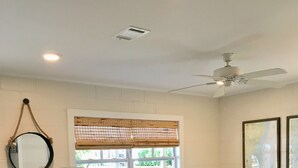 Ein Wohnzimmer mit einem weißen Sofa, einem Couchtisch, einer Lampe, einem Beistelltisch, einem Deckenventilator und einem Fenster mit Jalousien.