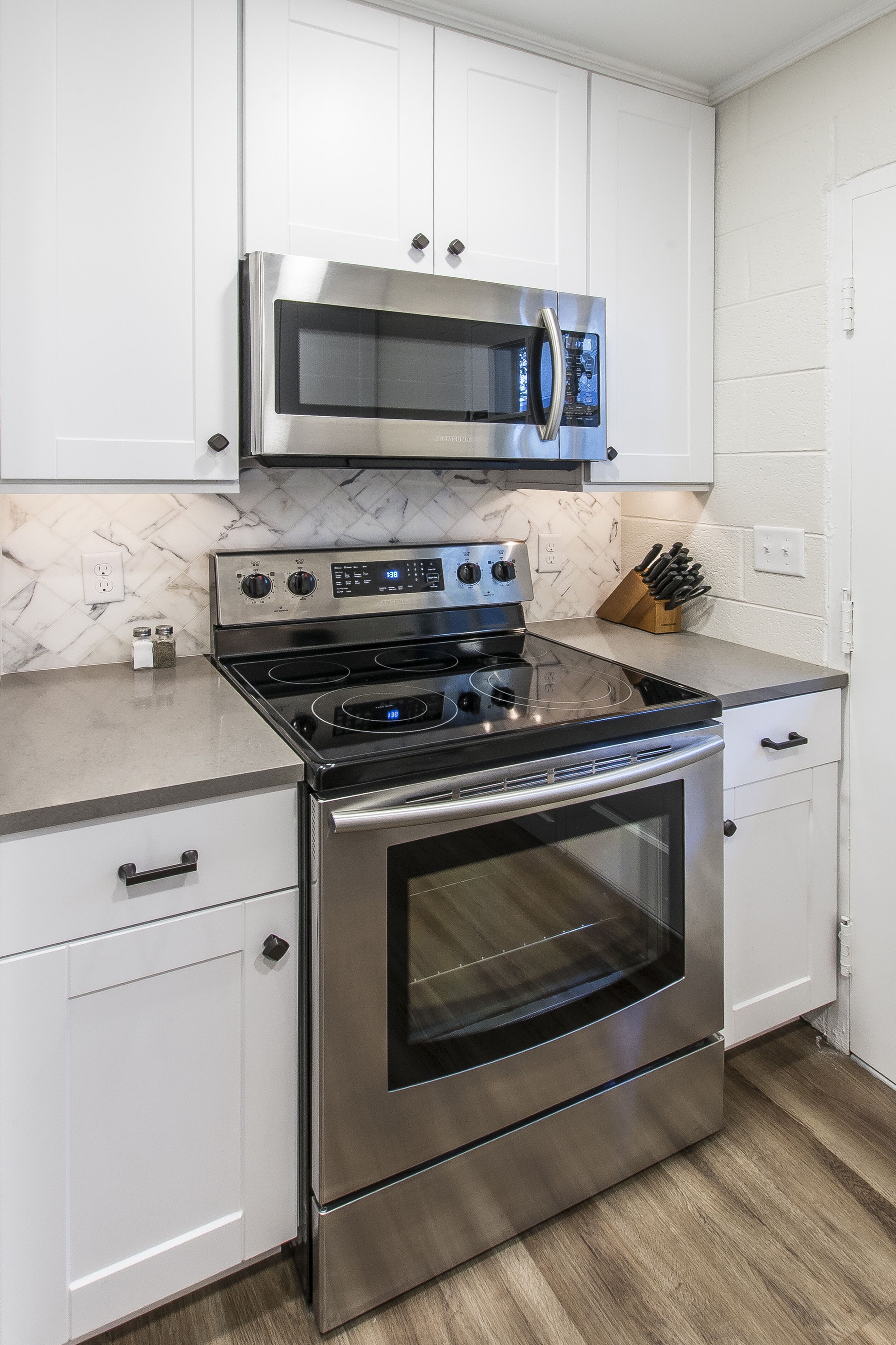 A kitchen with stainless steel appliances, white cabinetry, and a marble backsplash.