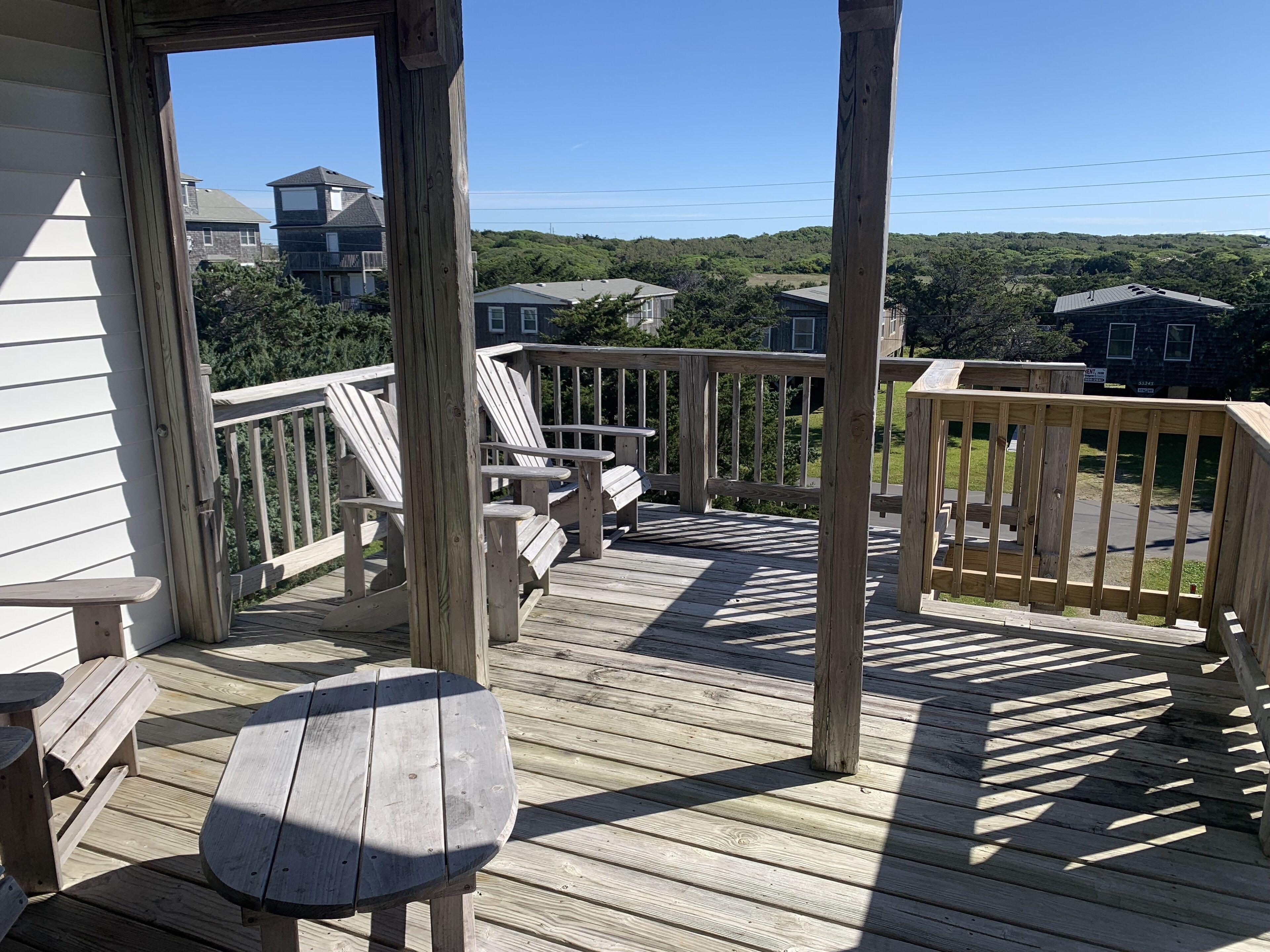 A wooden deck with a bench and chairs, overlooking a residential area with houses and greenery.