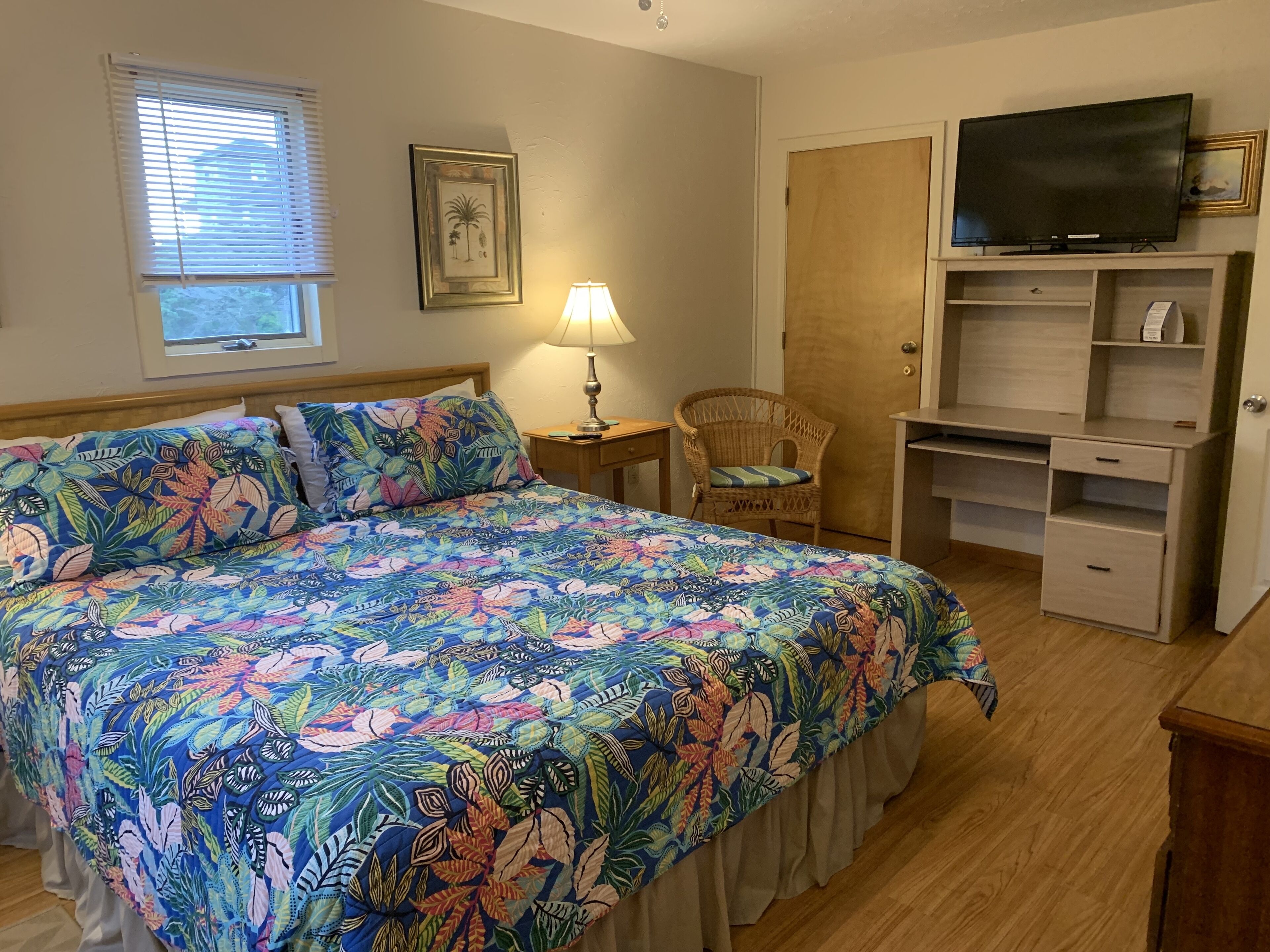 A bedroom with a large bed, a television on a shelf, a chair, and a desk.