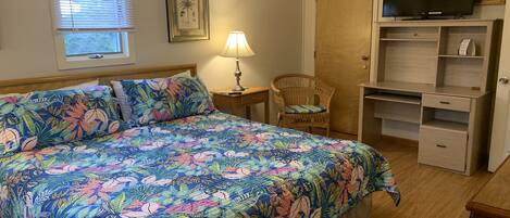 A bedroom with a large bed, a television on a shelf, a chair, and a desk.