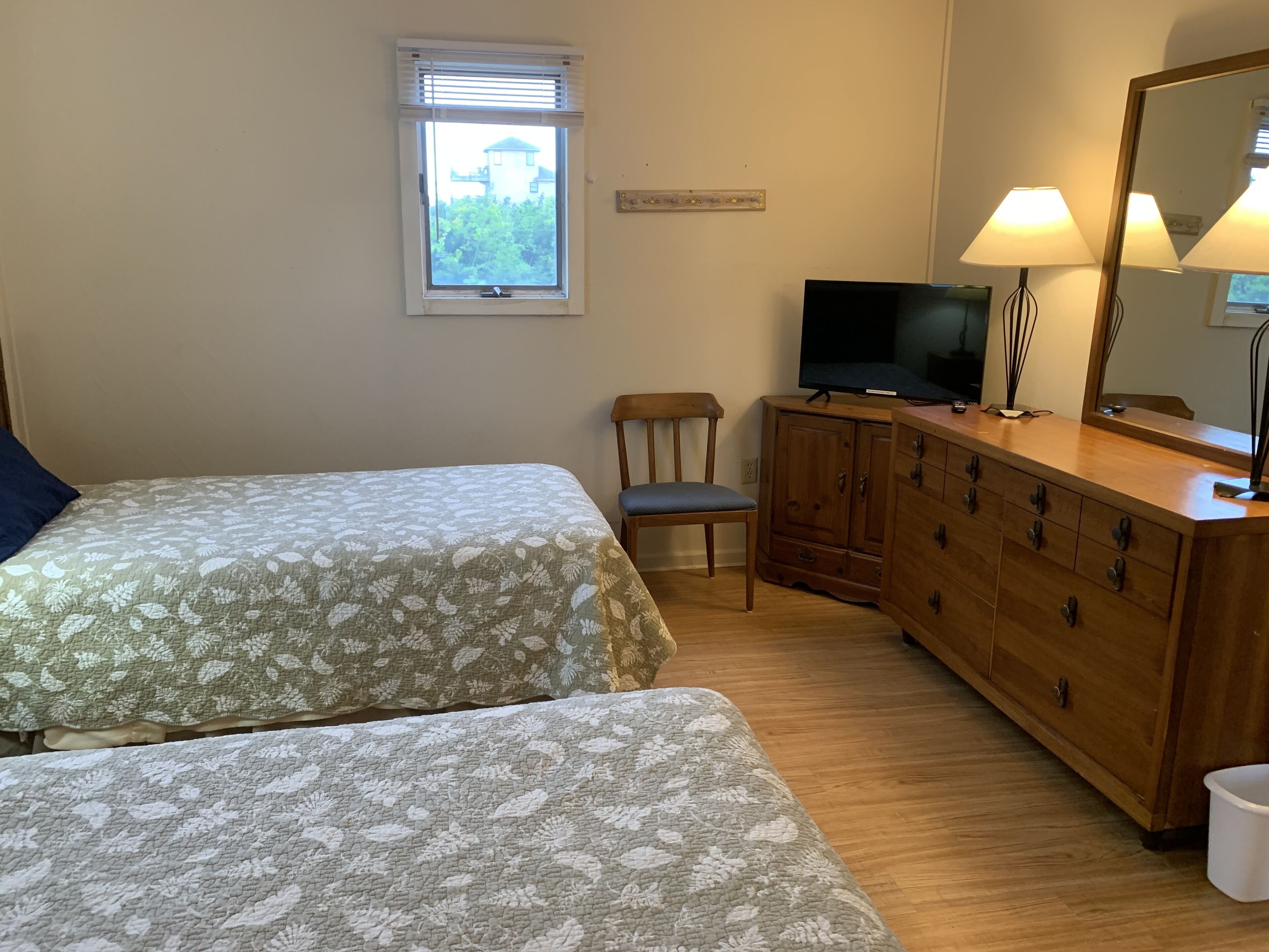 Une chambre avec deux lits, une commode en bois, un t éléviseur et une fenêtre avec des stores.