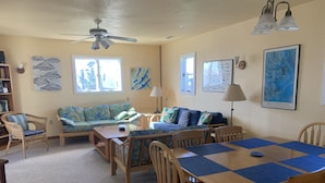 A cozy living room with a sofa, a dining table with chairs, a ceiling fan, and artwork on the walls. - Frisco Beach House! Some ocean views! Easy walk to the beach!  (Frisco)