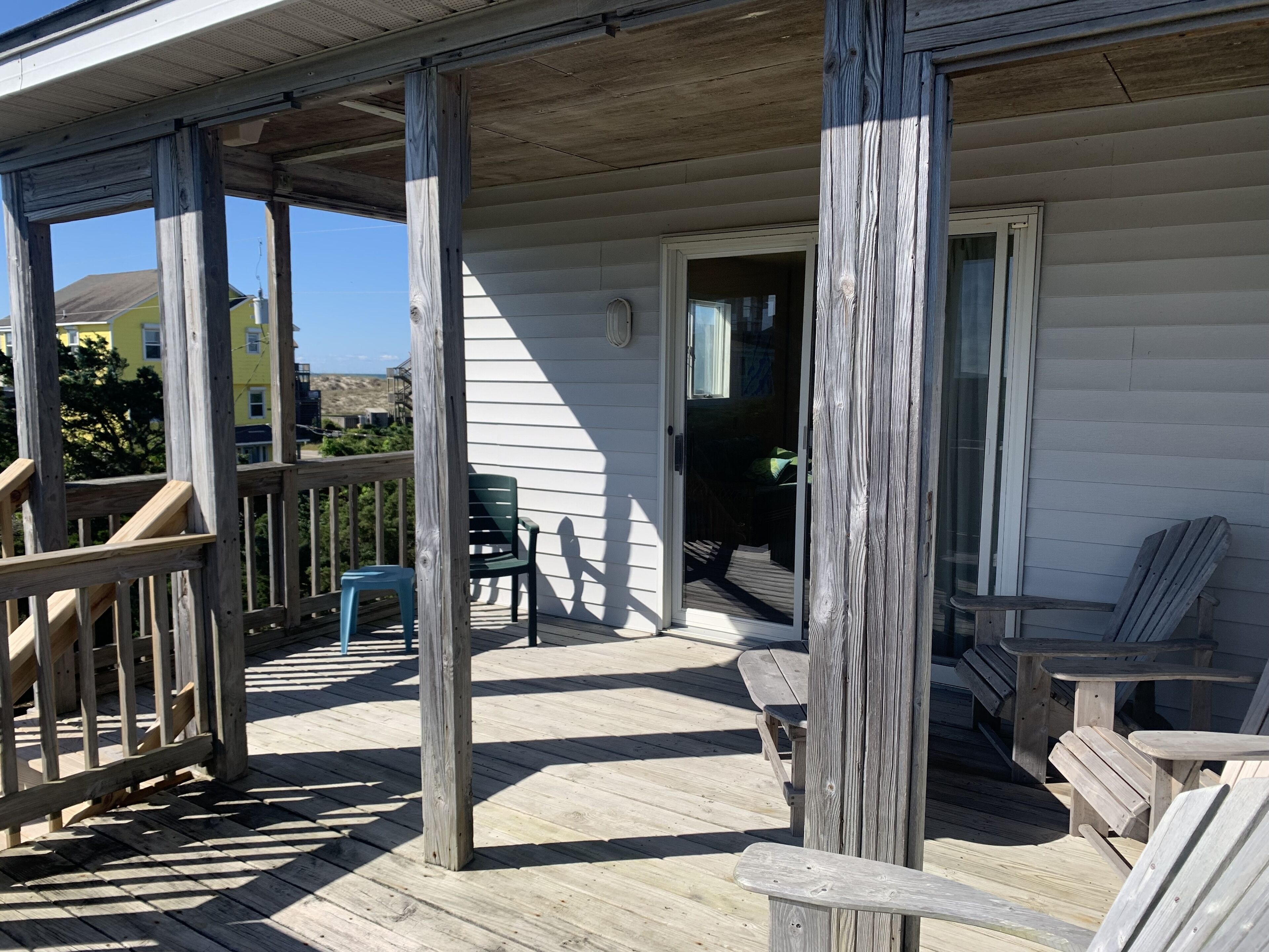 Une terrasse en bois dotée d’un porche abrité, de sièges d’extérieur et offrant une vue sur un bâtiment situé au loin.
