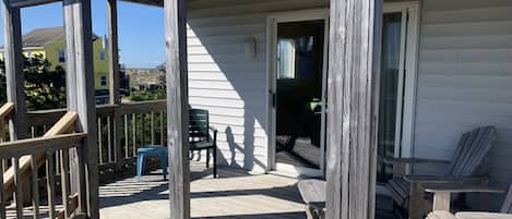 Une terrasse en bois dotée d’un porche abrité, de sièges d’extérieur et offrant une vue sur un bâtiment situé au loin.