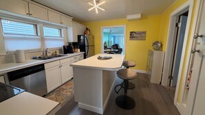 Una cocina con armarios blancos, un refrigerador negro, una cafetera y un taburete de bar.