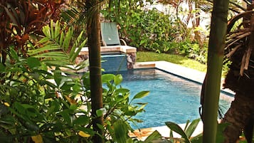 A pool surrounded by lush greenery and a stone structure.