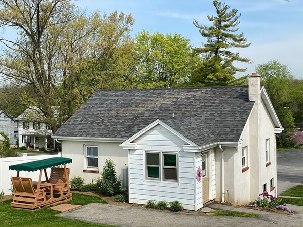 A single-story house with a gabled roof, a front porch with a green awning, and a small garden with flowers and shrubs. - Rent A Cottage On A Small farm (Paradise)