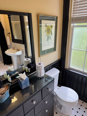 Un bagno con lavandino, specchio, water e un quadro appeso raffigurante un girasole.