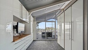 A corridor with a TV on a wooden shelf, leading to a glass door opening to a balcony with a view of boats and buildings. - Relax on Lake Pontchartrain (New Orleans)