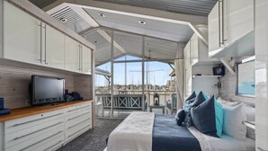 A modern, compact bedroom with a bed, bedside tables, and a TV. It features a balcony with a view of boats and a clear sky. - Relax on Lake Pontchartrain (New Orleans)