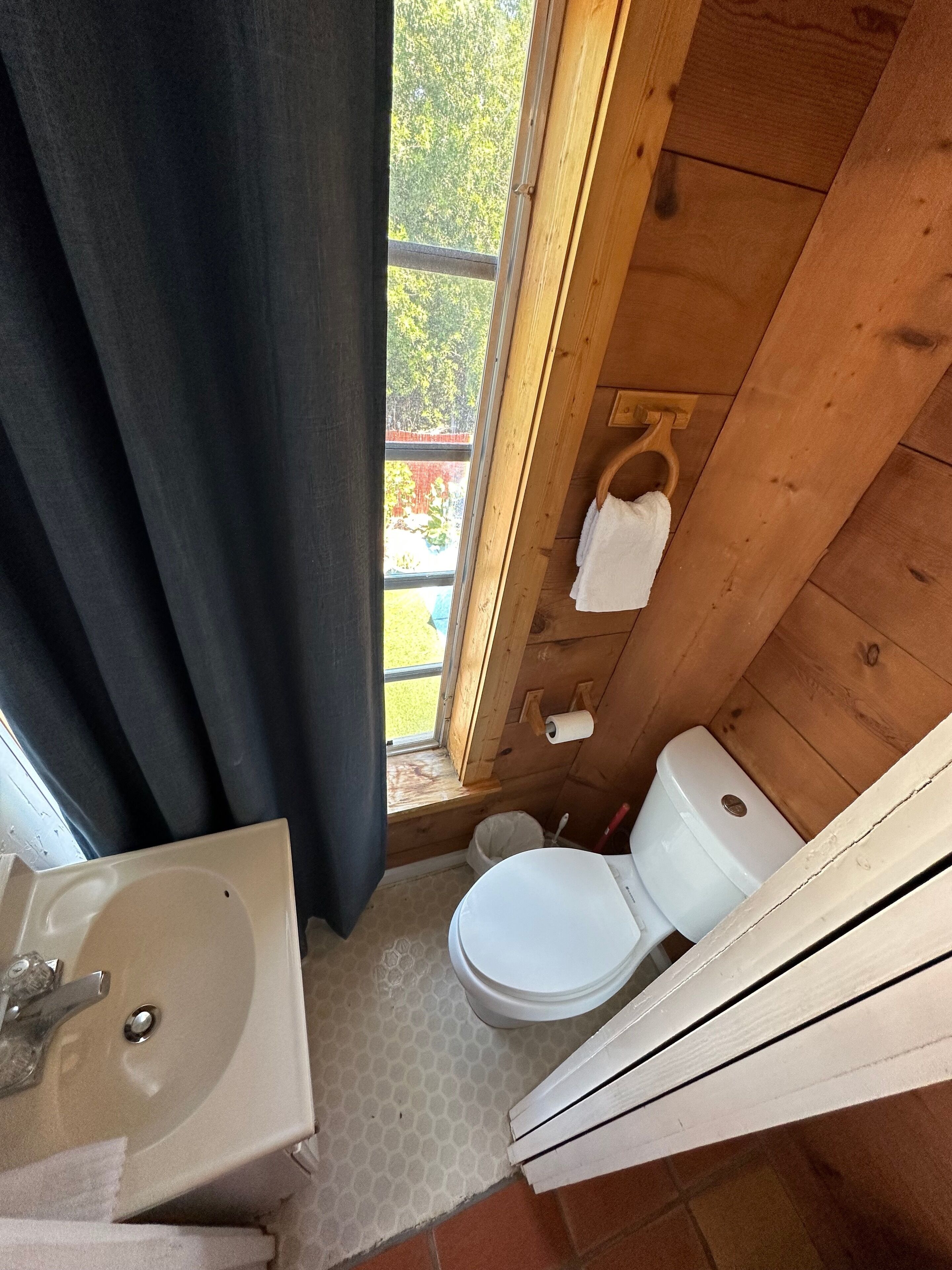 Une petite salle de bain en bois, équipée d’un lavabo, de toilettes et d’une fenêtre.