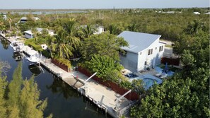 Luchtbeeld van een pand aan het water met een huis, aanlegsteiger en zwembad.