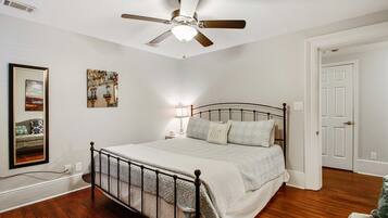 Un dormitorio con cama, ventilador de techo, mesita de noche y una puerta.