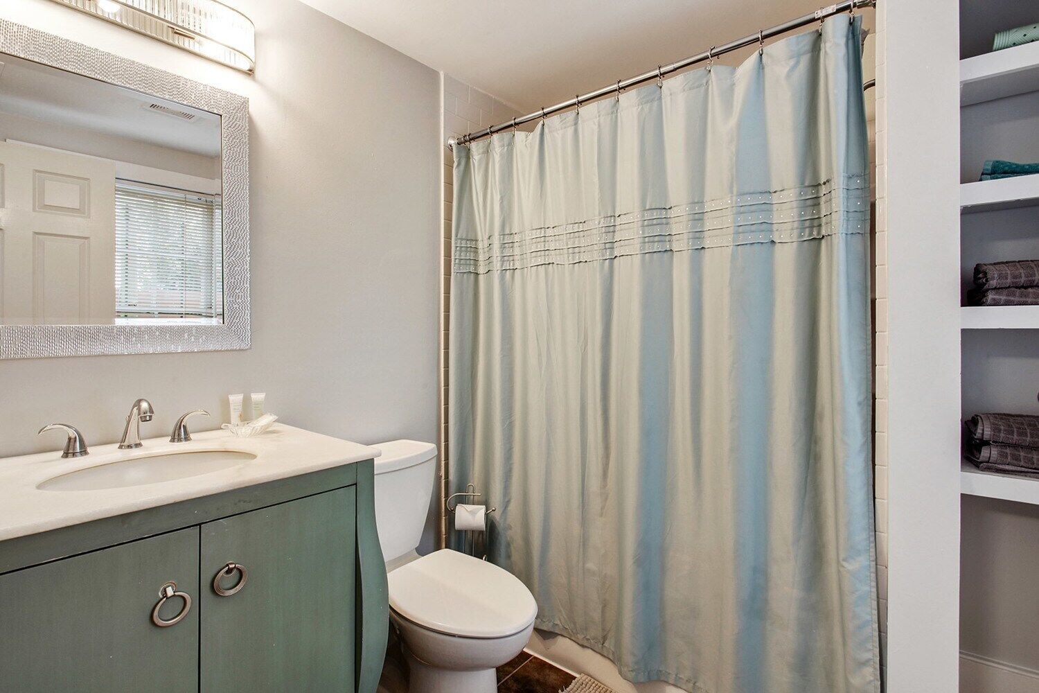 Un baño con lavamanos, espejo, inodoro y cortina de ducha.