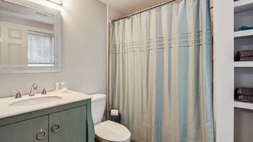 Un baño con lavamanos, espejo, inodoro y cortina de ducha.