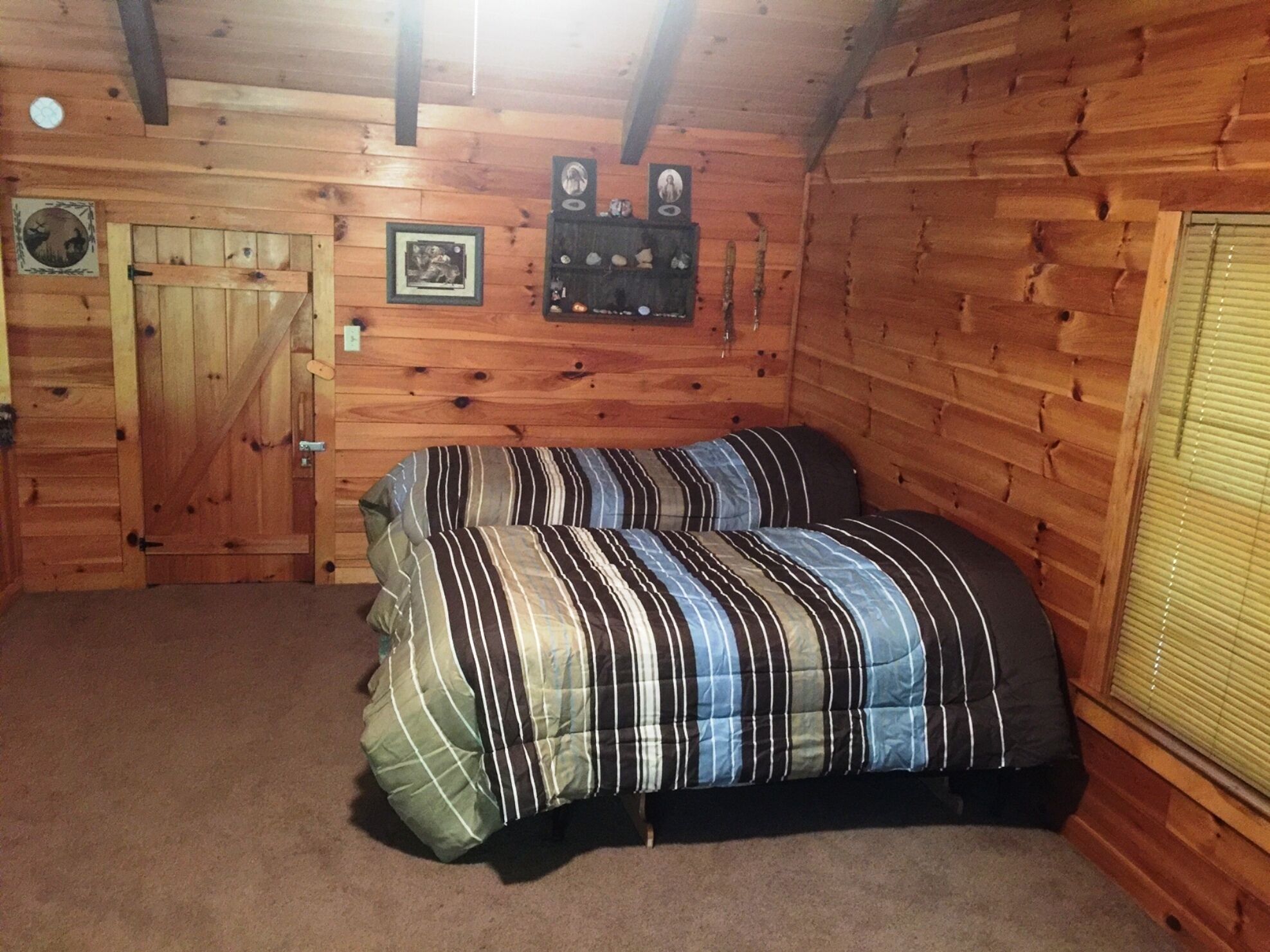 Ein Schlafzimmer in einer Blockhütte mit Bett, Holzwänden, einer Tür und einem Fenster mit Jalousien.