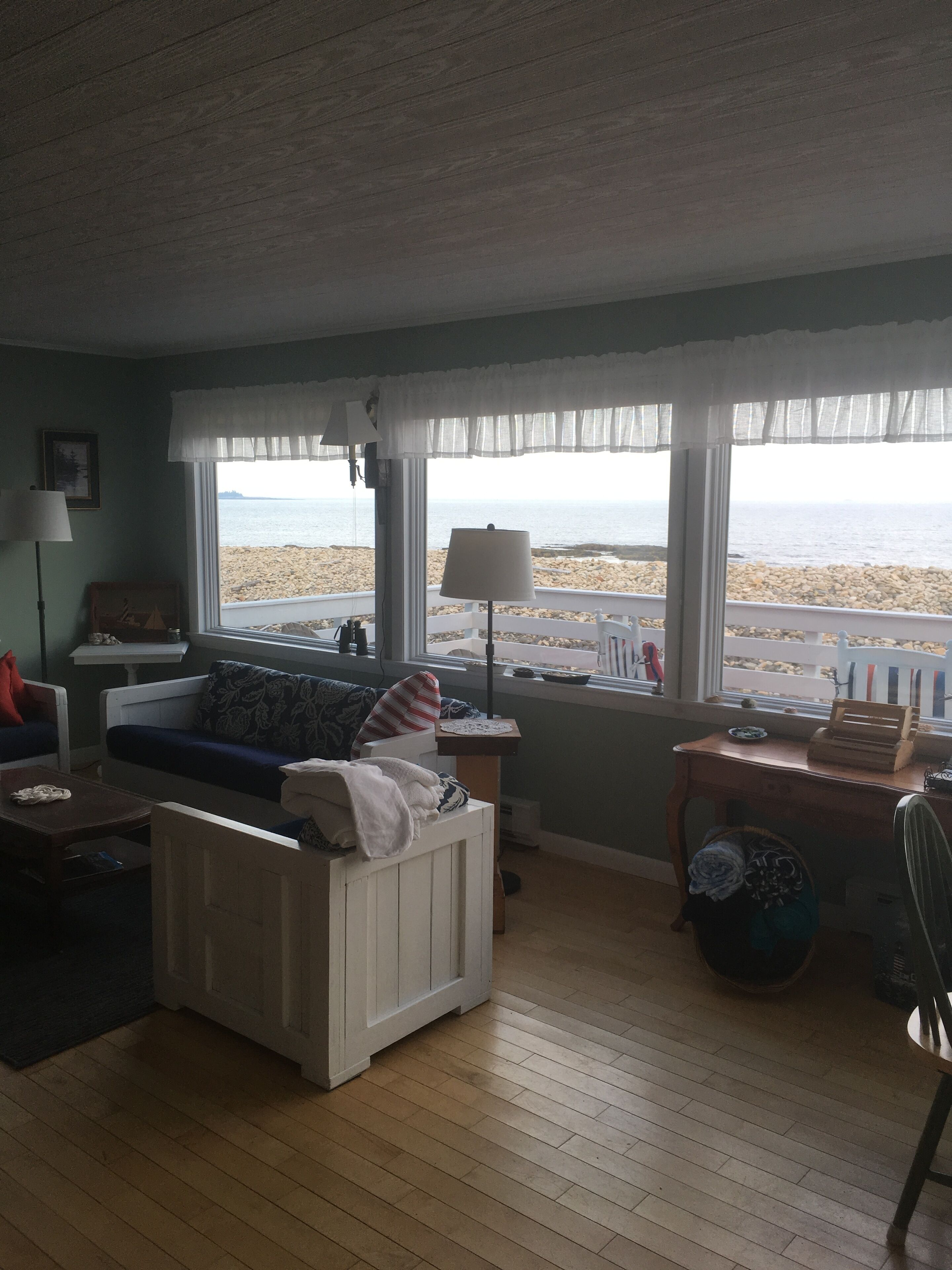 A room with a view of the sea, a white sofa, a table, and a lamp.