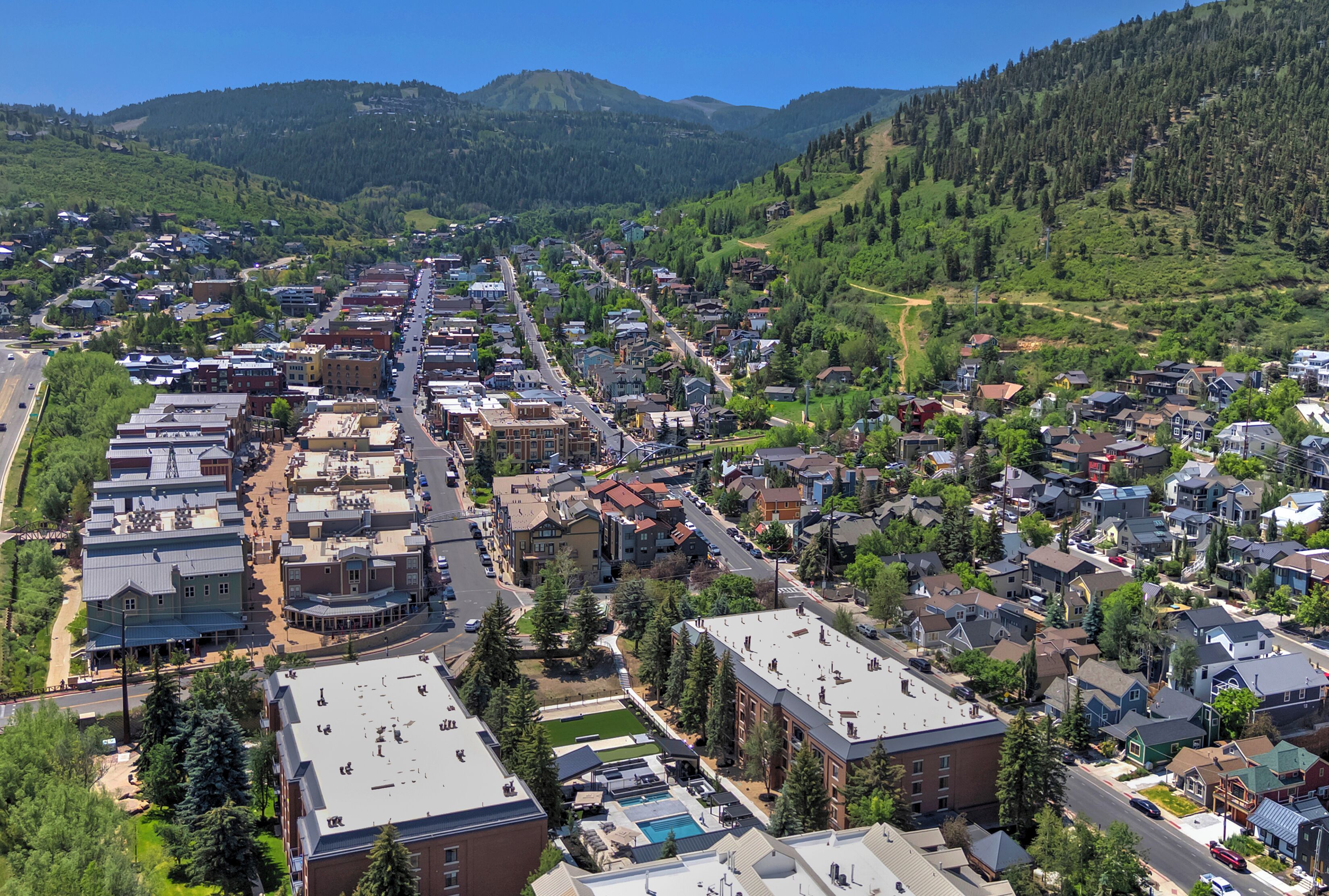 Un pueblo con una mezcla de edificios residenciales y comerciales, una calle principal y montañas al fondo.