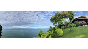 A coastal landscape with a house overlooking the sea, surrounded by lush greenery and a clear sky. - 4BR Oceanfront Luxury Villa • Private Estate • Spectacular Sunsets (Dominical)