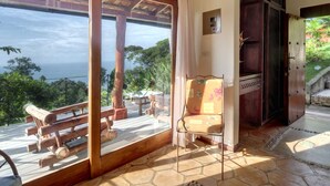 A room with a wooden deck, a chair with a floral cushion, and a view of the ocean. - 4BR Oceanfront Luxury Villa • Private Estate • Spectacular Sunsets (Dominical)