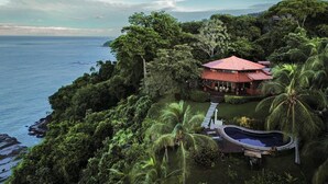 A secluded resort with a red-roofed pavilion, a swimming pool, and lush tropical vegetation. - 4BR Oceanfront Luxury Villa • Private Estate • Spectacular Sunsets (Dominical)
