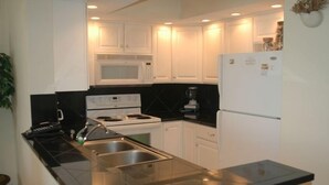 A modern kitchen with white cabinets, a black countertop, a stove, a sink, and a refrigerator.