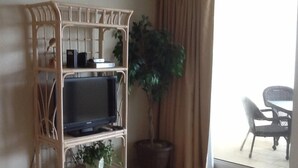 A living room with a television on a wooden stand, a potted plant, and a dining area with a table and chairs.
