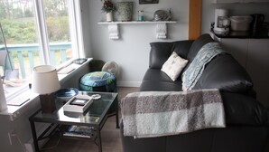 A living room with a dark leather sofa, a glass coffee table, a lamp, and a view of the outdoors through a window.