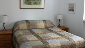 A bedroom with a large bed, two bedside tables with lamps, a framed painting on the wall, and a window.