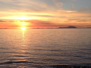 Un atardecer sobre un mar tranquilo con formas de tierra a lo lejos.