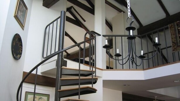 Una escalera de caracol con barandillas negras y escalones de madera, que conduce a un piso superior.