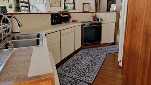Cocina compacta con horno integrado, cafetera y microondas. Hay una encimera de madera y un fregadero con escurreplatos.